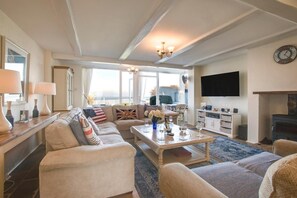 A spacious living room with a large sofa set, a coffee table, and a fireplace. There is a television mounted on the wall and a clock above it. - 3 Bed in Overstrand (oc-1795) (Overstrand)