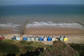 A beach with a row of colorful beach huts and a wooden jetty extending into the sea. - 3 Bed in Overstrand (oc-1795) (Overstrand)