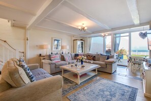A spacious living room with a sofa set, a coffee table, and a dining area with a table and chairs. There is a large window providing a view of the outdoors. - 3 Bed in Overstrand (oc-1795) (Overstrand)
