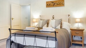 En pænt redt seng med sengegavl, to sengeborde med lamper og et maleri på væggen.