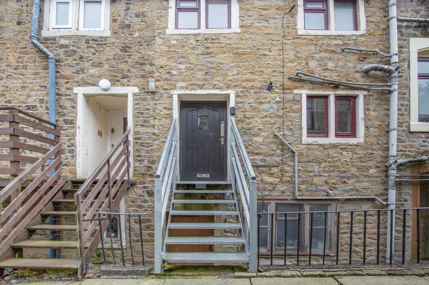 A stone building with a central door, wooden stairs, and a metal railing.