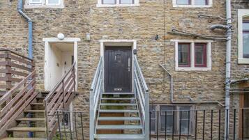 A stone building with a central door, wooden stairs, and a metal railing.