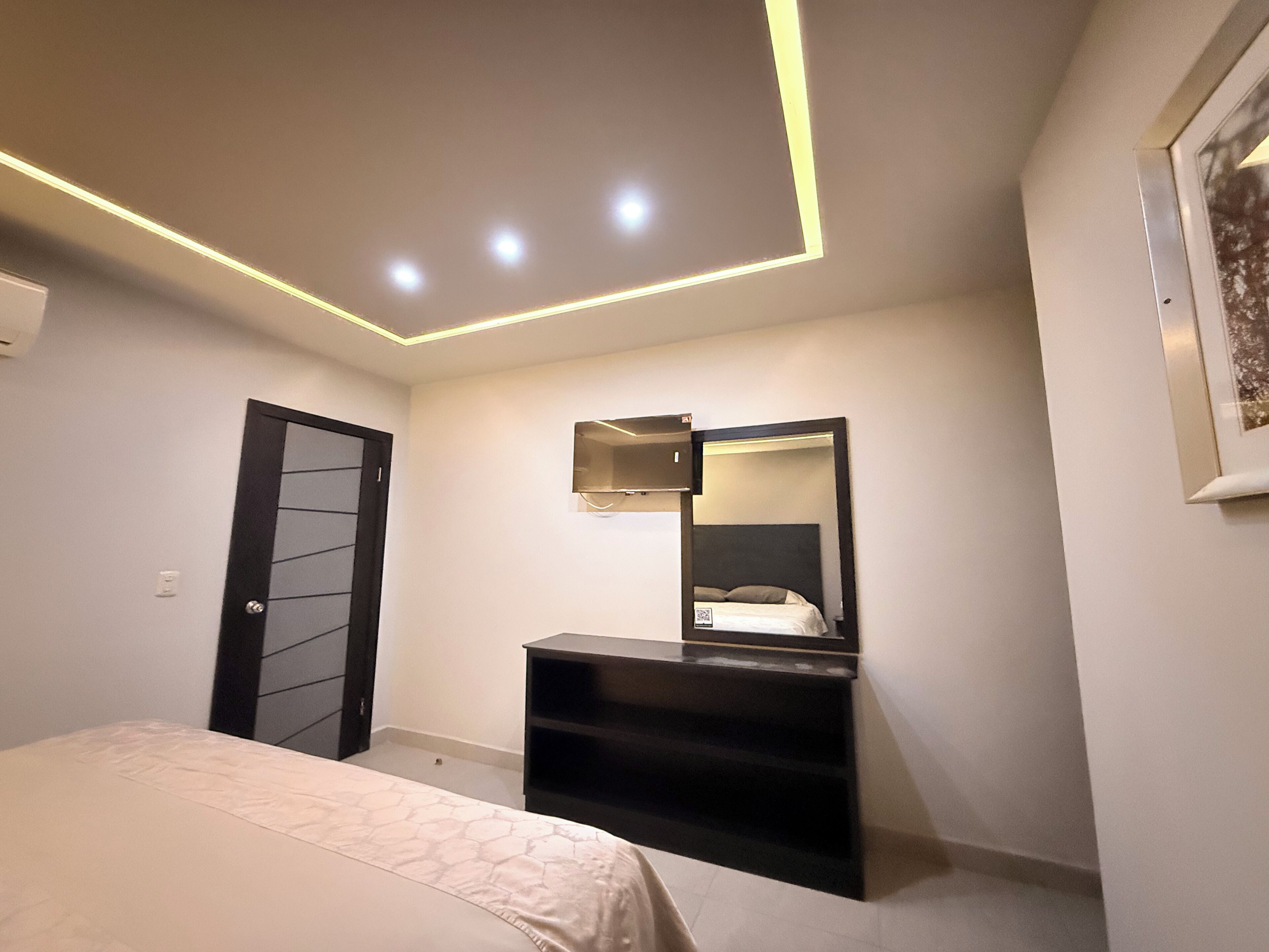 A bedroom with a bed, a dresser, a mirror, and recessed ceiling lighting.