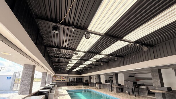Uma área interna de piscina moderna, com piscina curva, pilares de pedra e teto com claraboias.