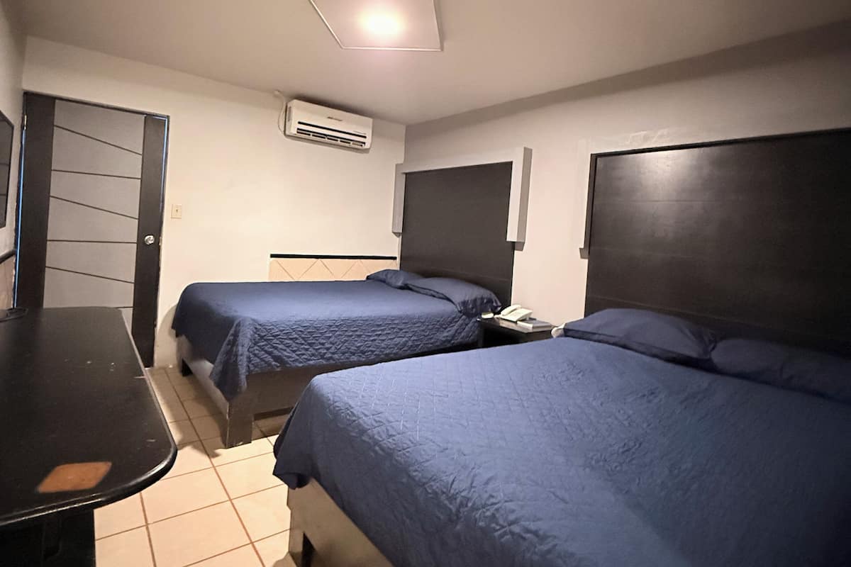 A hotel room with two beds, a desk, and a chair.