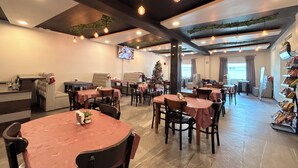 Um restaurante com mesas redondas, cadeiras e um pinheiro de Natal.