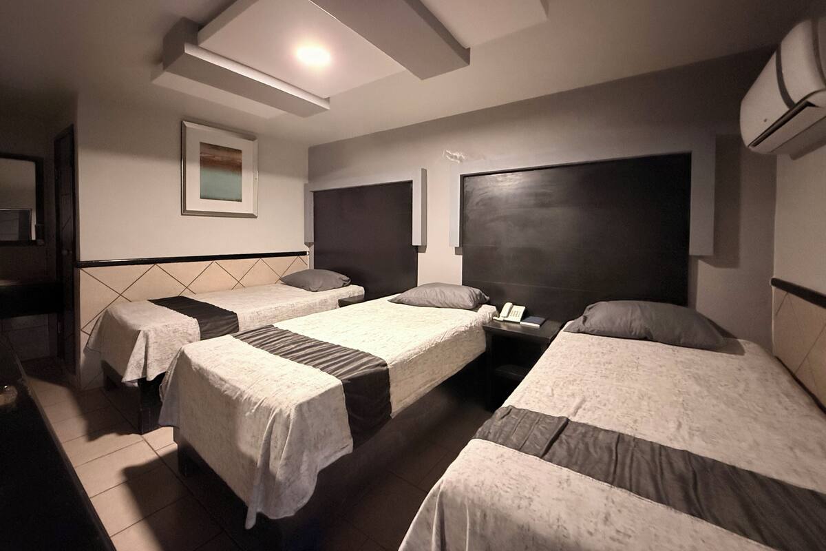 A hotel room with three single beds, a bedside table with a phone, and a small window.