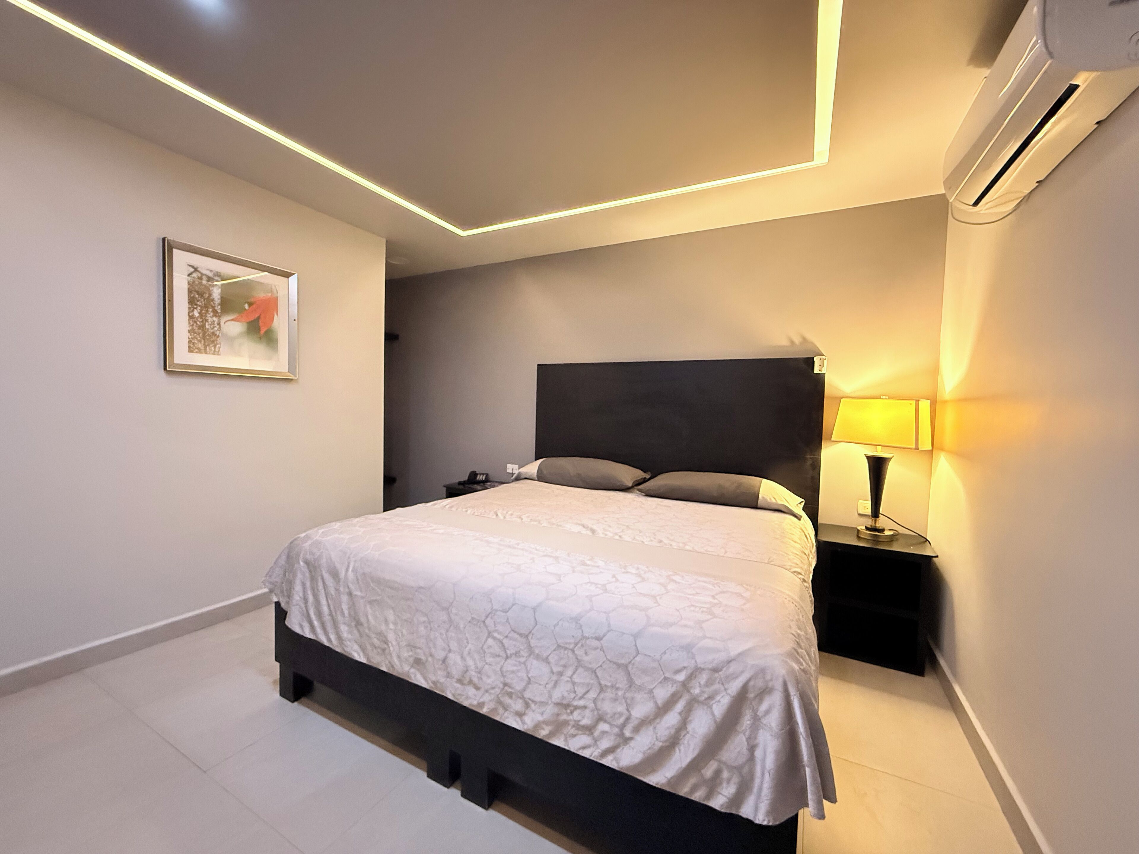 A modern bedroom with a bed, bedside table, lamp, and an air conditioning unit.