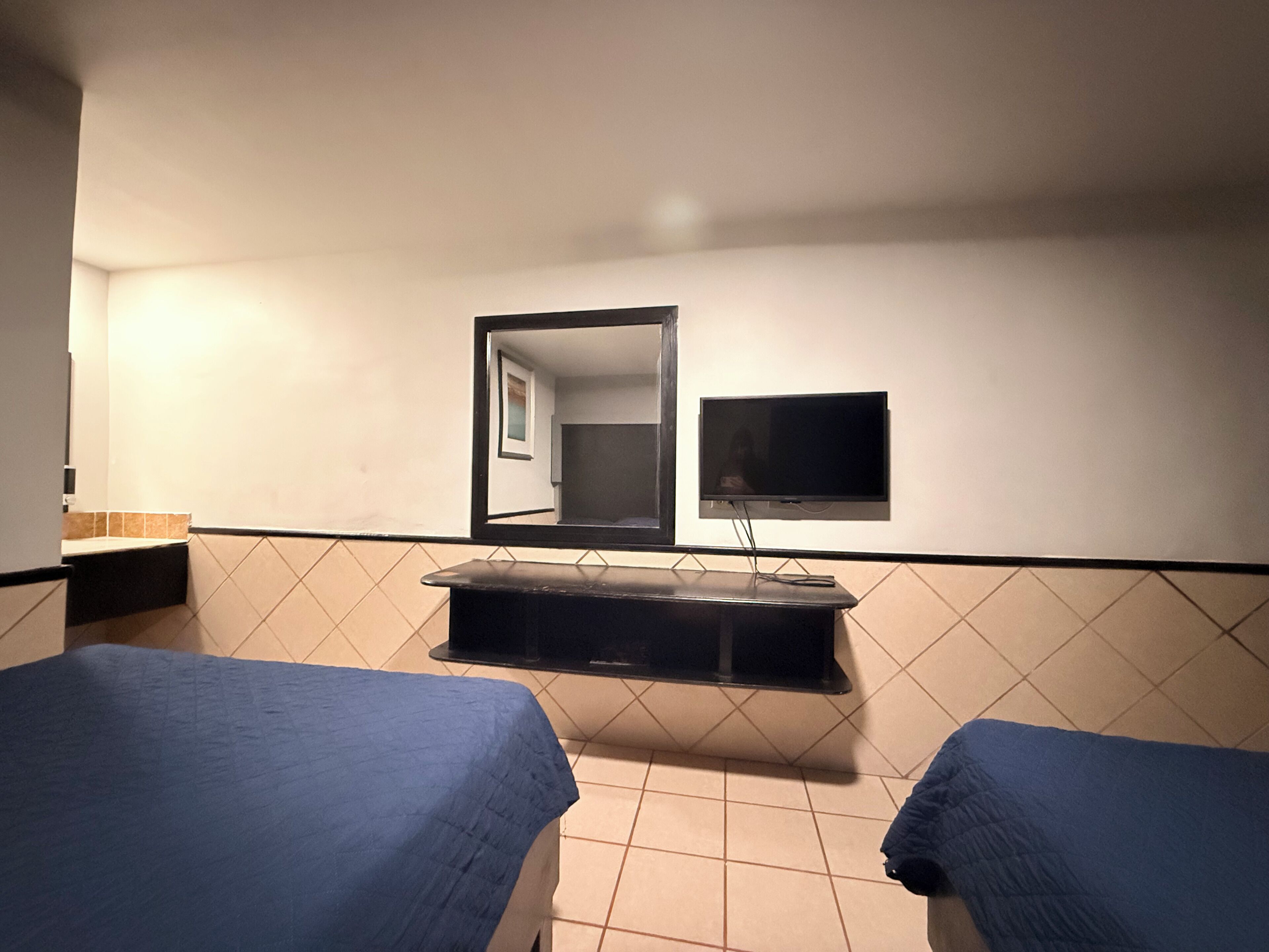 Una habitación de hotel con dos camas, un televisor y un espejo.