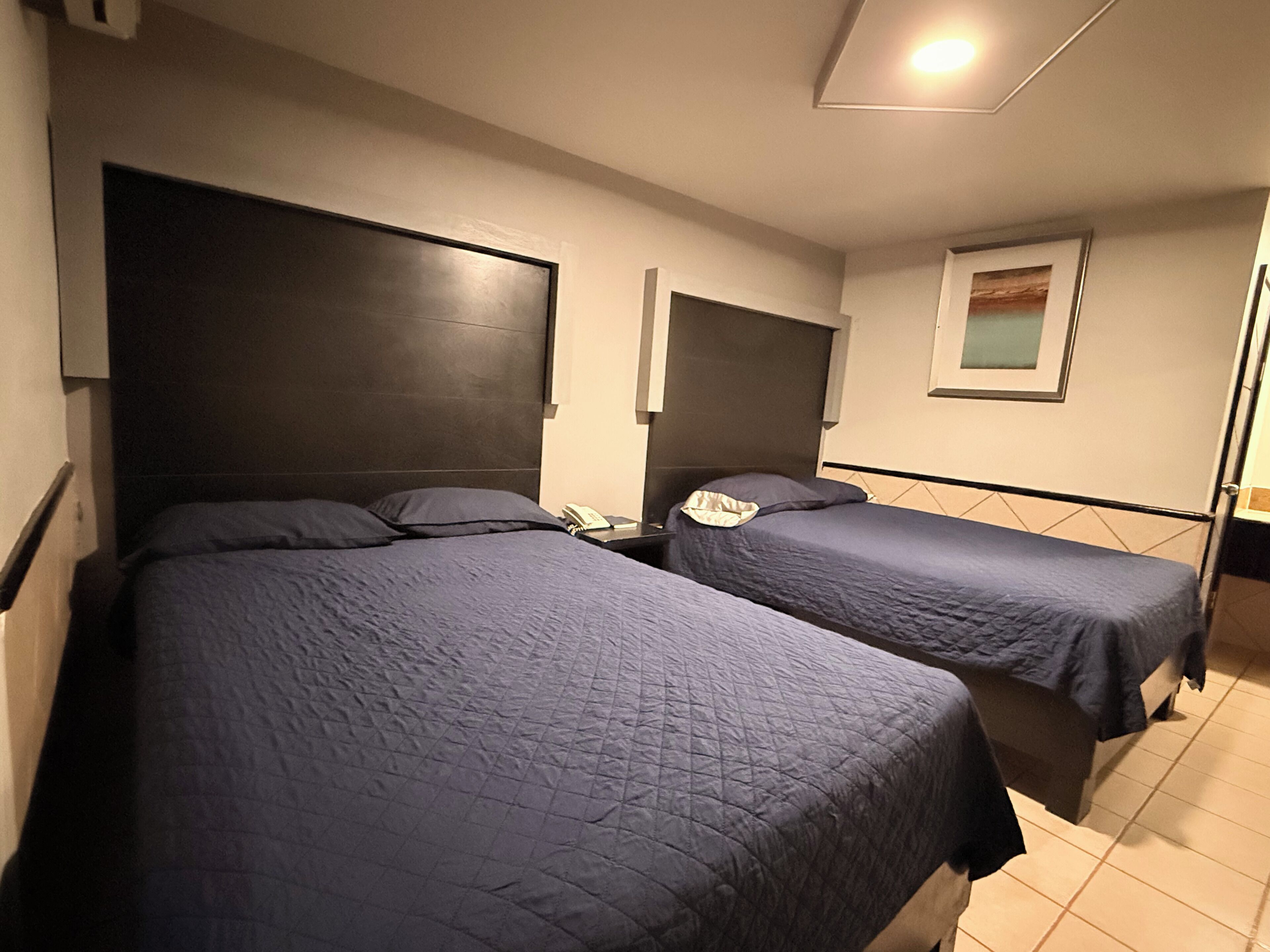 A hotel room with two beds, each with a headboard and a bedside table.