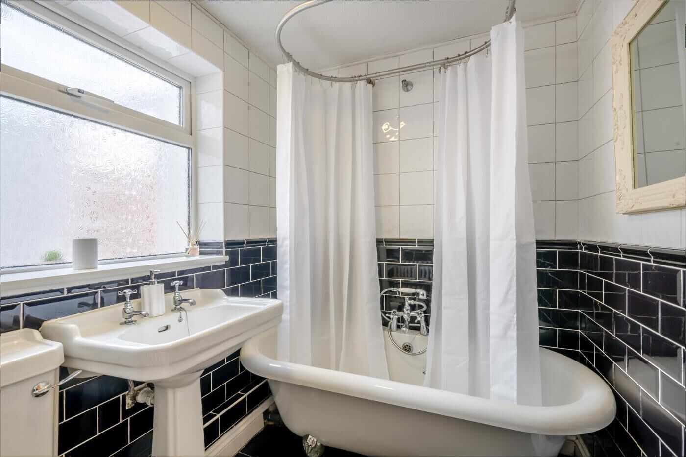 A bathroom with a freestanding bathtub, a window with frosted glass, and black and white tiled walls.