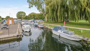 Un canale con barche ormeggiate, un piccolo edificio in mattoni e un salice piangente.