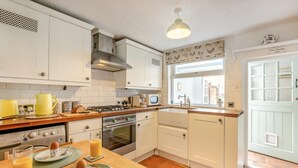 Cucina con mobili bianchi, piano cottura a gas, forno, microonde e finestra vista esterna.