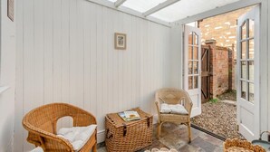 Una veranda coperta con mobili in vimini, un tavolino e una porta che dà su uno spazio esterno con un muro in mattoni.