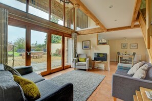 A spacious living area with a large sliding glass door leading to a garden, a comfortable seating area with sofas and a TV, and a dining area with a table and chairs. - 3 Bed in Thursford (oc-1793) (Thursford)