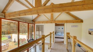 Eine Holztreppe führt zu einem Schlafzimmer mit Bett und Blick auf einen Garten durch große Fenster.