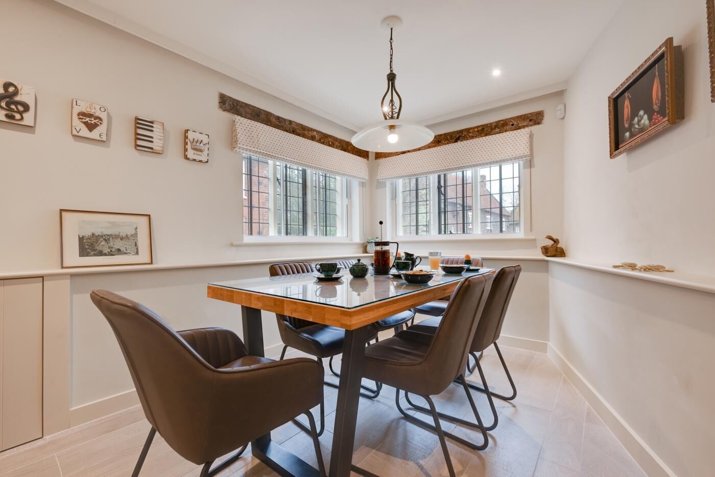 A dining area with a glass table, four chairs, a hanging light fixture, and a window with blinds.