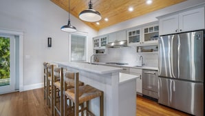 A modern kitchen with a central island, stainless steel appliances, and a wooden ceiling. - Spacious Beachfront Home in Holmes Beach on Anna Maria Island! Swell Life (Holmes Beach)