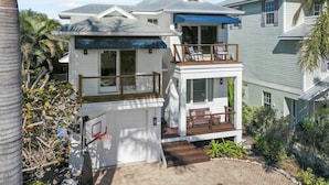 A two-story house with a balcony, a basketball hoop, and a small deck with outdoor seating. - Spacious Beachfront Home in Holmes Beach on Anna Maria Island! Swell Life (Holmes Beach)