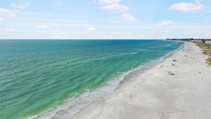 A beach with clear turquoise water, a sandy shore, and a few umbrellas. - Spacious Beachfront Home in Holmes Beach on Anna Maria Island! Swell Life (Holmes Beach)