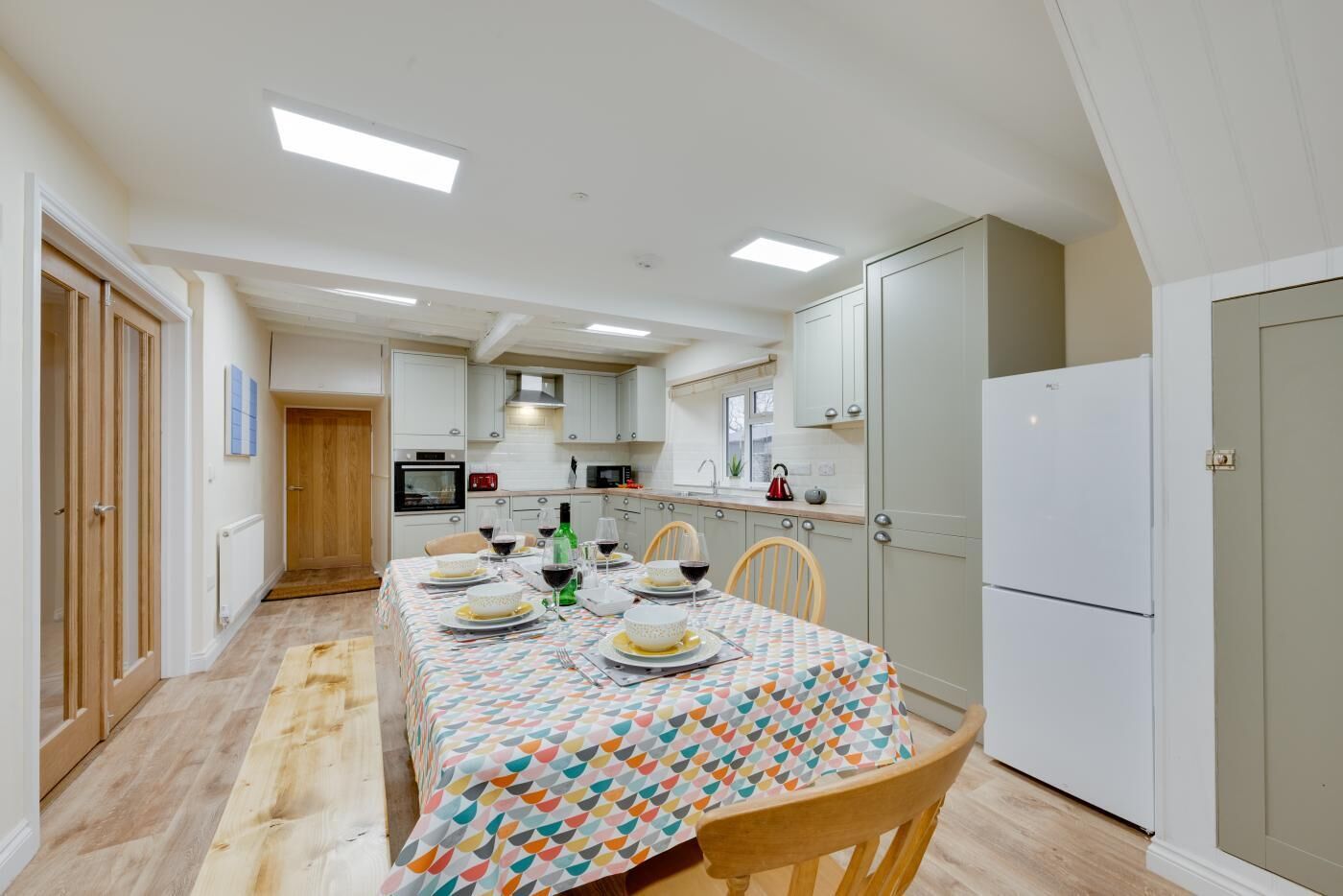 A modern kitchen with white cabinets, a dining table set for four, and a refrigerator.