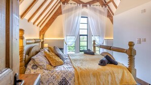 Un dormitorio con techo de madera, una cama con ropa de cama estampada, una ventana con cortinas de encaje y una mesita de noche.