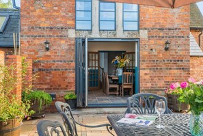 Un bâtiment en briques doté d’un patio, d’un espace extérieur avec des sièges et d’une table à manger avec des chaises.