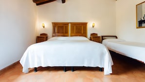 Ein Schlafzimmer mit einem großen Bett, einem kleineren Bett, einem Holz-Kopfteil, zwei Nachttischen und einem Spiegel an der Wand.