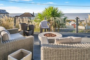A wicker outdoor seating area with a fire pit, overlooking a beach. - 5 Bed in Ogmore-by-Sea (oc-o33570) (Ogmore-by-Sea)