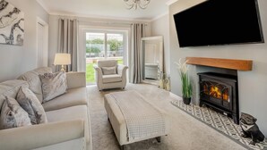 Un salon comprenant un canapé, un fauteuil, un pouf, une cheminée, un téléviseur et une vue sur l’extérieur.