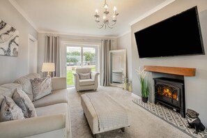 A living room with a sofa, armchair, ottoman, fireplace, TV, and a view of the outdoors. - 3 Bed in Pentlepoir (oc-a33527) (Saundersfoot)