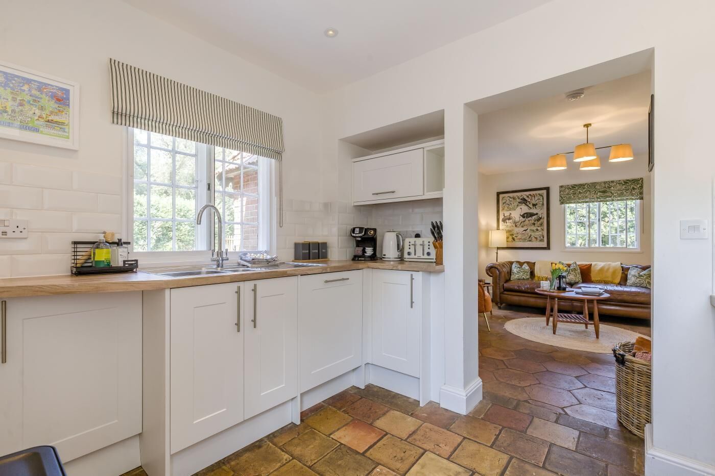 A modern kitchen with white cabinets, a wooden countertop, and a window with striped valance.