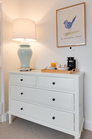 A white dresser with a lamp, a framed bird illustration, and breakfast items. - 2 Bed in Wells-next-the-Sea (oc-2229) (Wighton)