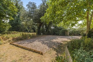 A garden with a gravel area and wooden borders, surrounded by dense greenery and trees. - 2 Bed in Wells-next-the-Sea (oc-2229) (Wighton)