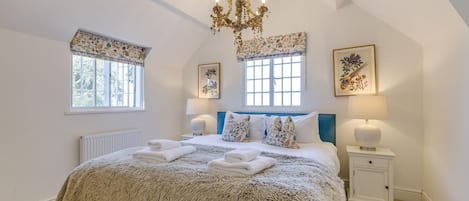A bedroom with a large bed, two bedside tables, a chandelier, and two windows with curtains.
