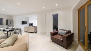 A modern living room with a sofa, a dining table, and a TV mounted on the wall. - 4 Bed in Saundersfoot (oc-493314) (Saundersfoot)