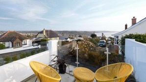 A balcony with wicker chairs, a potted plant, and a view of the town. - 4 Bed in Saundersfoot (oc-493314) (Saundersfoot)
