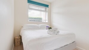 A neatly made bed with white linens, a small bedside table with a lamp, and a window with blinds. - 1 Bed in Langland (oc-hh1423) (Newton)
