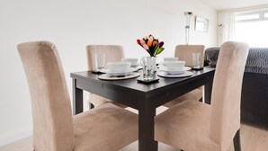 A dining table with chairs, a vase of flowers, and a lamp in a room with a sofa and a window. - 1 Bed in Langland (oc-hh1423) (Newton)
