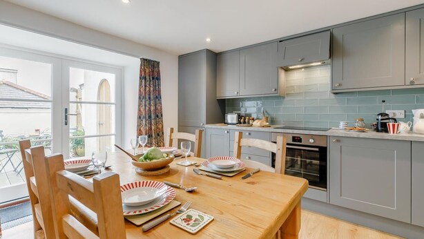Een moderne keuken met grijze kastjes, een houten eettafel gedekt voor vier personen en een uitzicht op het buitenlands landschap door een groot raam.