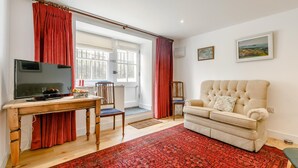 Een woonkamer met een televisie, een bank, een rode vloerkleed en een raam met gordijnen.