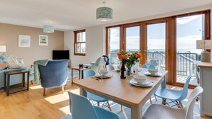 En moderne stue med spiseplads, store vinduer og en balkon med udsigt.