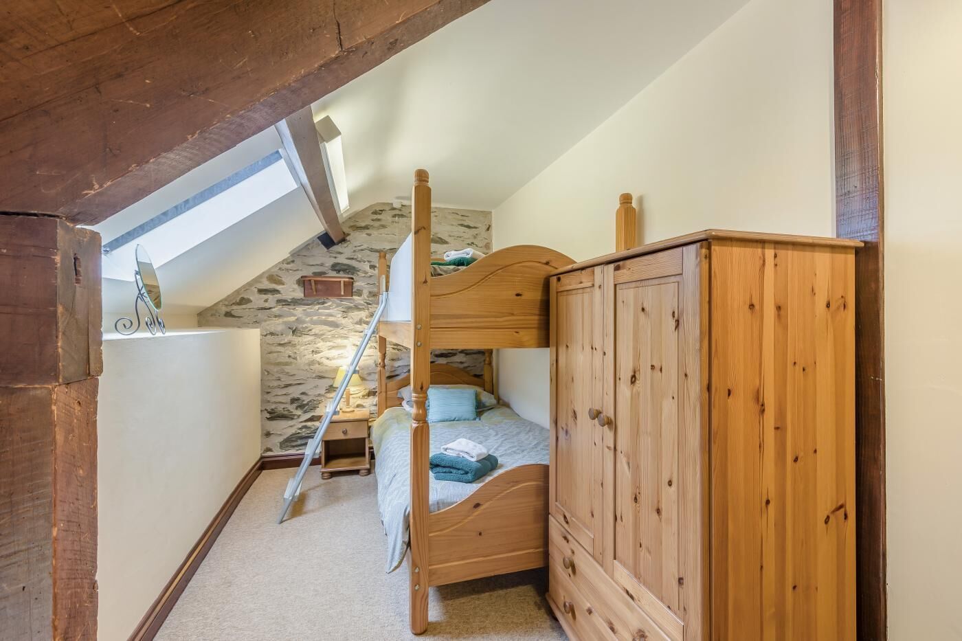 Une chambre avec un lit superposé, une armoire en bois, un mur en pierre et une lucarne.