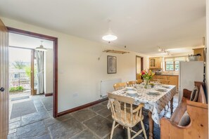A dining area with a table set for four, a bench, and a kitchen in the background. - 4 Bed in Builth Wells (oc-39461) (Cilmery)