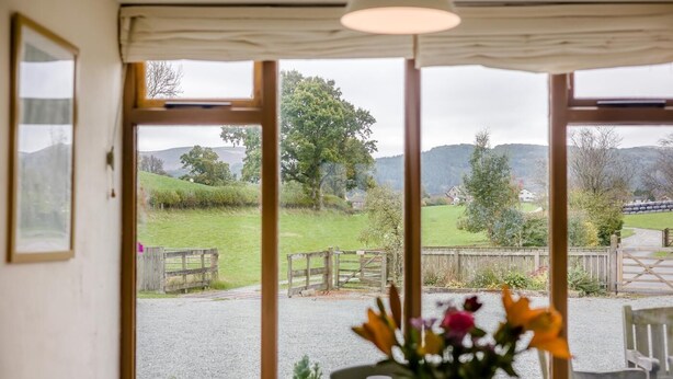 Ein Zimmer mit großen Fenstern, einer Holztür und Blick auf eine ländliche Landschaft.