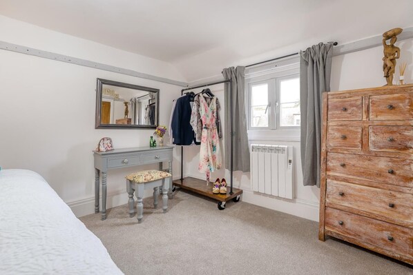 A bedroom with a bed, a vanity with a mirror, a dresser, and a window with curtains.