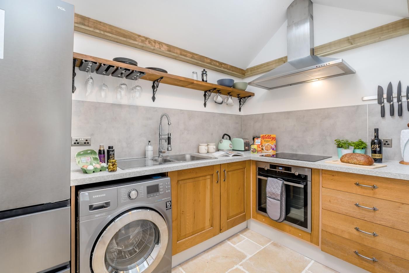 Une cuisine compacte équipée d’un lave-linge, d’un four encastré et de meubles de rangement en bois.