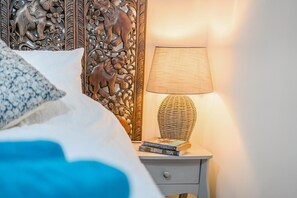 A neatly made bed with a patterned pillow, a bedside table with a lamp and books, and a decorative wall panel.