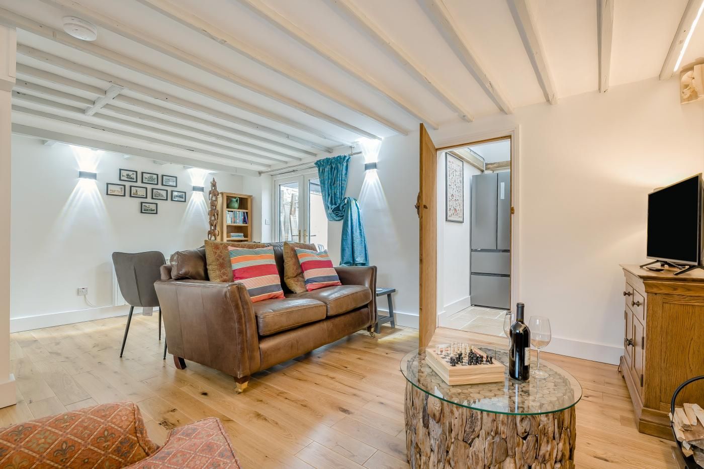 A spacious living room with a brown leather sofa, a glass coffee table, and a wooden cabinet.