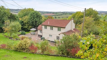 A two-story house with a red-tiled roof, surrounded by lush greenery and a well-maintained lawn.